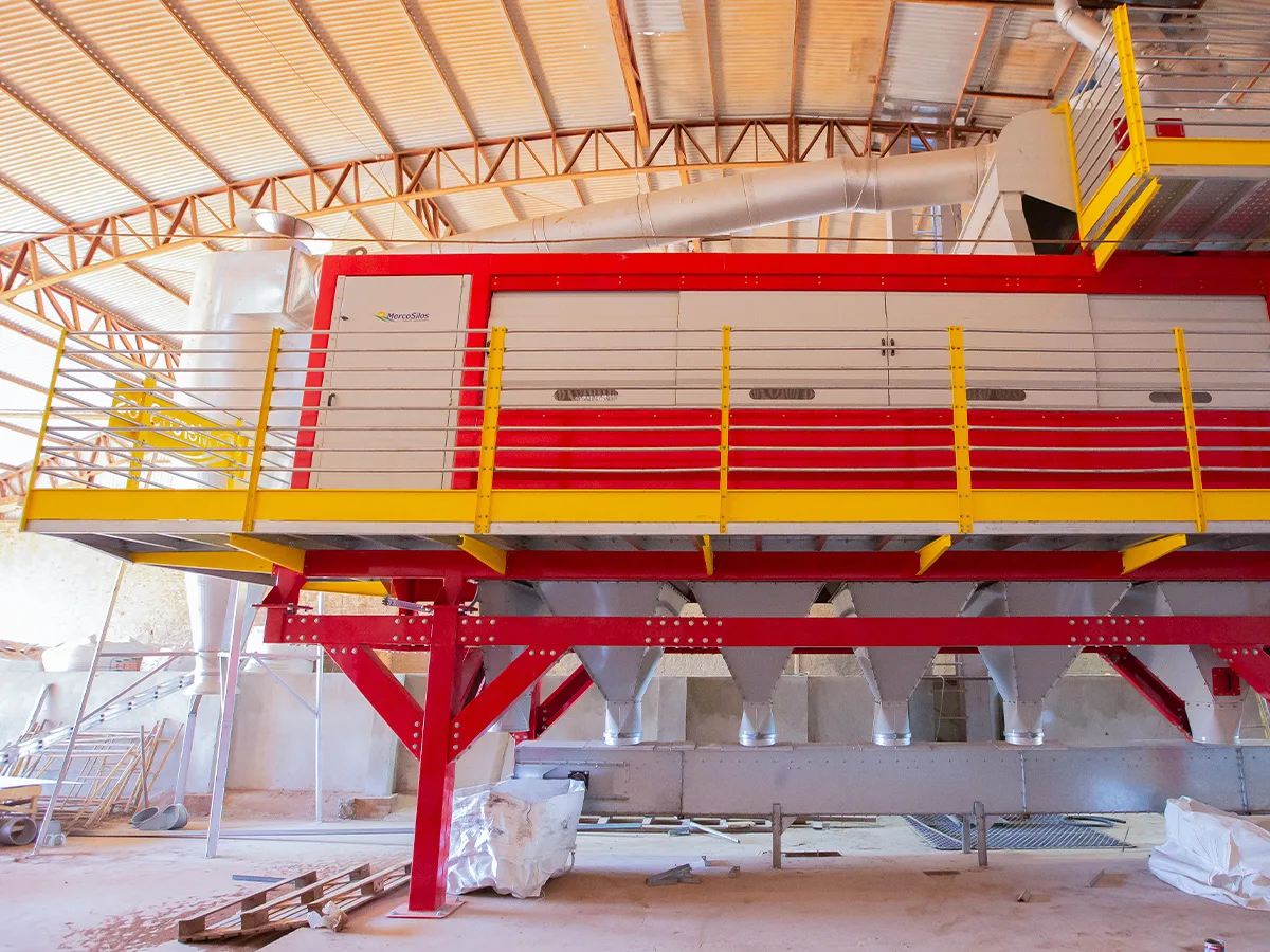 Maquina de limpeza de graos MercoSilos em vermelho e branco, instalada sobre plataforma com guarda-corpo amarelo