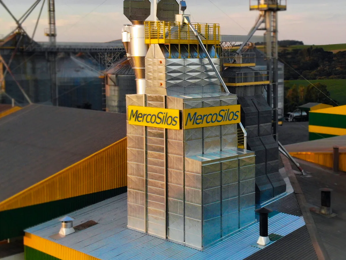 Secador MercoSilos visto de cima ao lado de silos metalicos e barracao com telhado amarelo e verde